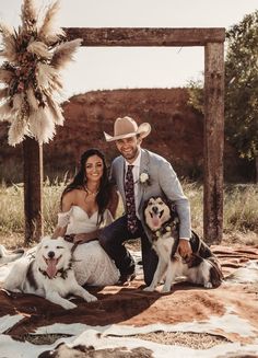 a bride and groom pose with their dogs in front of an old wooden frame for a photo