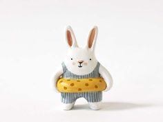 a white rabbit holding a piece of bread in its hands and wearing a sweater with polka dots on it