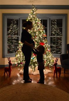 a woman and her child standing in front of a christmas tree with lights on it