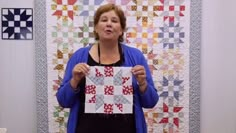 a woman holding up a piece of paper in front of a quilted wall hanging