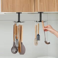 kitchen utensils hanging from the wall with wooden cabinets in the background and a woman's hand holding a spoon