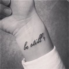 a woman's wrist tattoo with the word be still on it, in cursive font