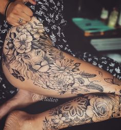 a woman's leg with flowers and a lion tattoo on her arm, sitting in a chair