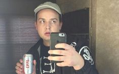 a man taking a selfie with his cell phone and beer in front of him