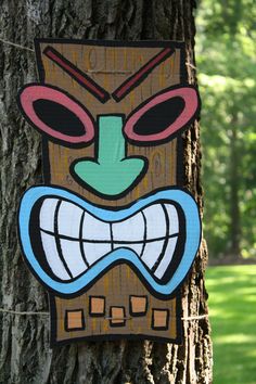 a tree trunk with a colorful mask on it's face hanging from the bark