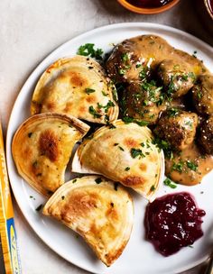 a white plate topped with dumplings covered in gravy next to dipping sauce