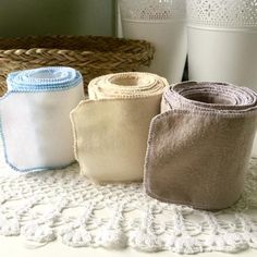 three rolls of toilet paper sitting on top of a doily next to two cups