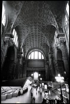 people are walking around in an old train station with high ceilings and arched glass windows