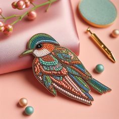 a colorful bird brooch sitting on top of a pink satin bag next to pearls