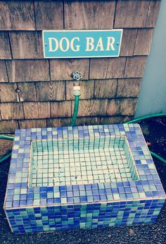 a blue and white tile bench sitting in front of a wooden building with a dog bar sign above it