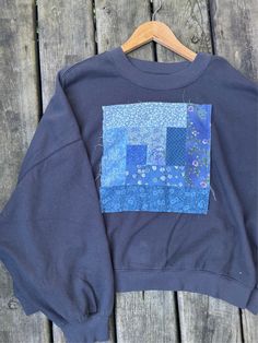 a blue sweatshirt with patchwork on it sitting on a wooden table next to a hanger