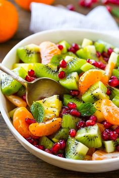 a white bowl filled with fruit salad on top of a wooden table next to oranges