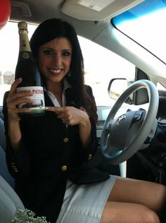 a woman sitting in the driver's seat of a car holding a bottle of wine