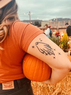 a woman with a tattoo on her arm holding a pumpkin in front of some hay