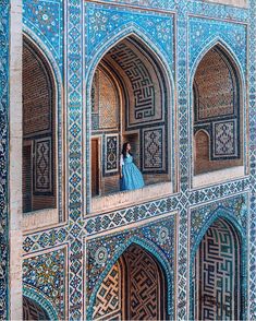 a woman in blue dress standing on the balcony of an ornate building with arches and doorways