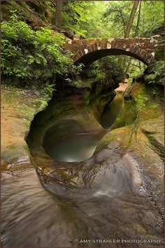 a stream running under a stone bridge in the woods