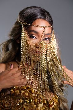 a woman with gold chains on her face and hands around her neck, wearing a golden dress