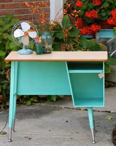 an old desk is painted blue and has some flowers in it on the side walk