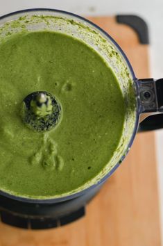 a blender filled with green liquid on top of a wooden cutting board