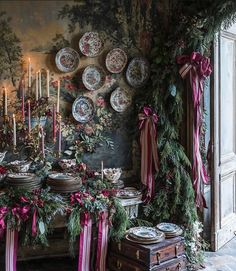 a dining room table with plates and candles on it, decorated for christmas time in front of a wall full of wreaths