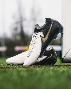 a pair of black and gold nike soccer cleats sitting on the grass in front of a white wall