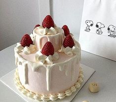 a white cake with strawberries on top sitting on a table next to buttons and a bag