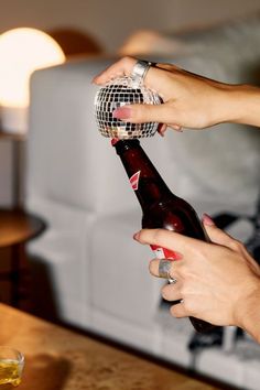 two hands holding a bottle with a disco ball on it