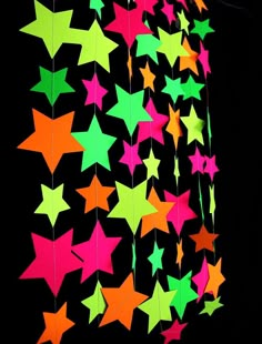 a bunch of stars hanging from the side of a black wall with neon green, pink and orange colors