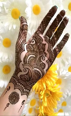 a hand with henna on it and yellow flowers in the foreground next to it