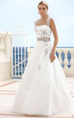 a woman in a white wedding dress standing on a balcony near the ocean with her hand on her hip