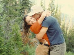 a man and woman hugging each other in the woods