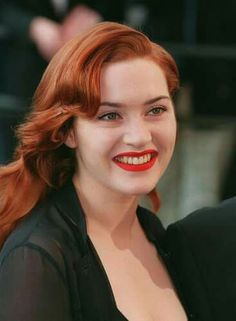 a woman with red hair is smiling at the camera while standing next to a man