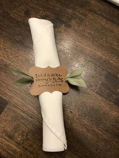 a napkin wrapped in white paper with a green ribbon and tag attached to it on a wooden table