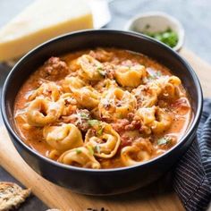 a black bowl filled with pasta and meat soup on top of a wooden cutting board