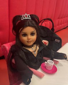 a doll sitting at a table with a bag and cup