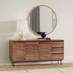 a wooden dresser with a round mirror above it and a lamp on the sideboard