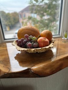 a bowl filled with fruit sitting on top of a wooden table next to a window