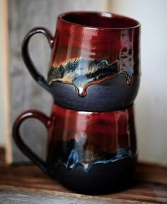 two red and black mugs sitting on top of a wooden table