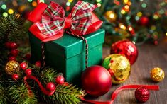 a green gift box with a red bow on it surrounded by christmas decorations and baubles