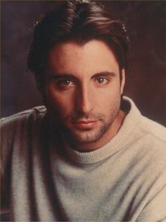 a man with long hair wearing a white sweater looking at the camera and posing for a photo