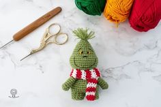 a crocheted green stuffed animal next to yarn and scissors on a marble surface