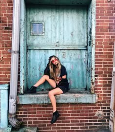 a woman sitting on a window sill in front of a blue door with her legs crossed