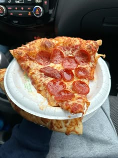 a slice of pepperoni pizza on a paper plate in someone's car seat