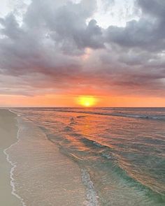 the sun is setting over the ocean with waves coming in