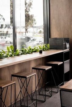 an empty restaurant with tables and stools in front of the window, along with potted plants