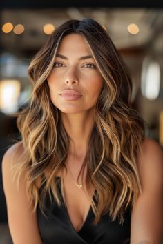 Portrait of a woman with wavy hair and subtle makeup smiling slightly against a softly blurred background. Caramel Partial Highlights, Balyage Hair, Braid Videos, 2023 Hair, Caramel Balayage