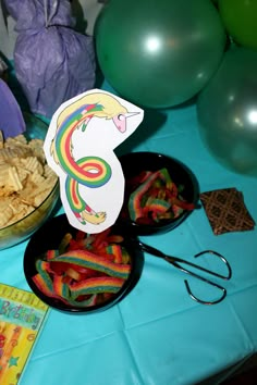 a table topped with plates and bowls filled with food next to green balloons on top of a blue table cloth