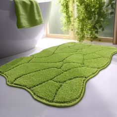 a green rug is on the floor in front of a white bathtub and window