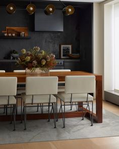 a dining room table with white chairs and flowers on it in front of a window