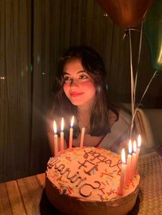 a woman sitting in front of a birthday cake with lit candles on it and balloons